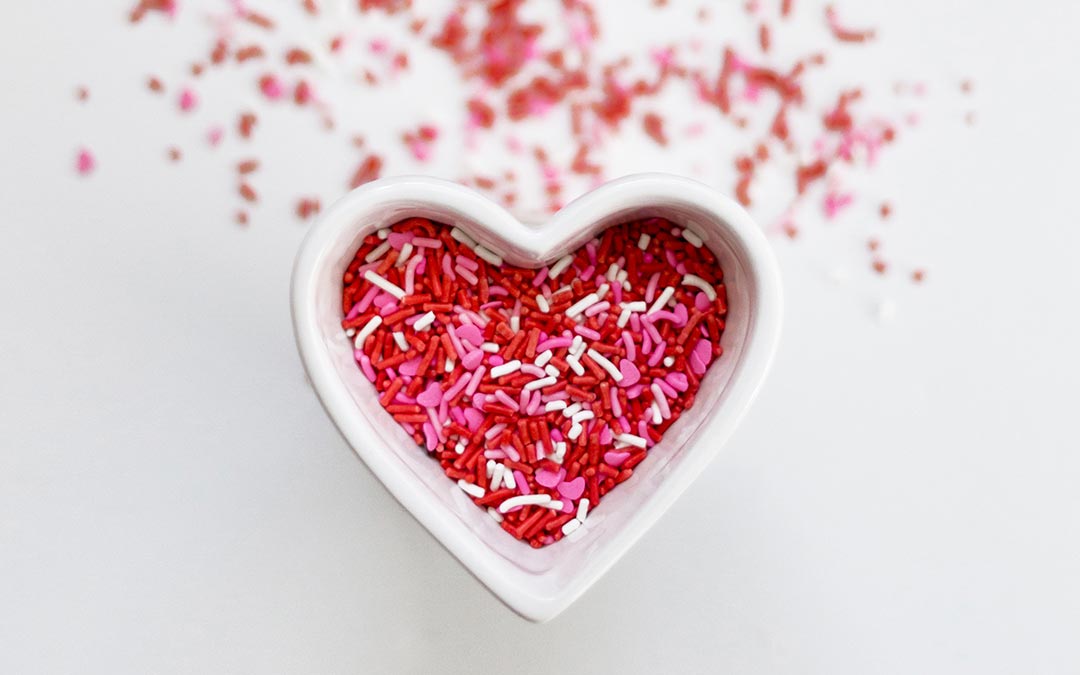 Red and pink sprinkles in a heart shaped bowl as part of the history Valentine's Day.