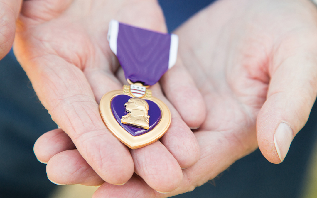 Hands holding a Purple Heart badge for Purple Heart Day